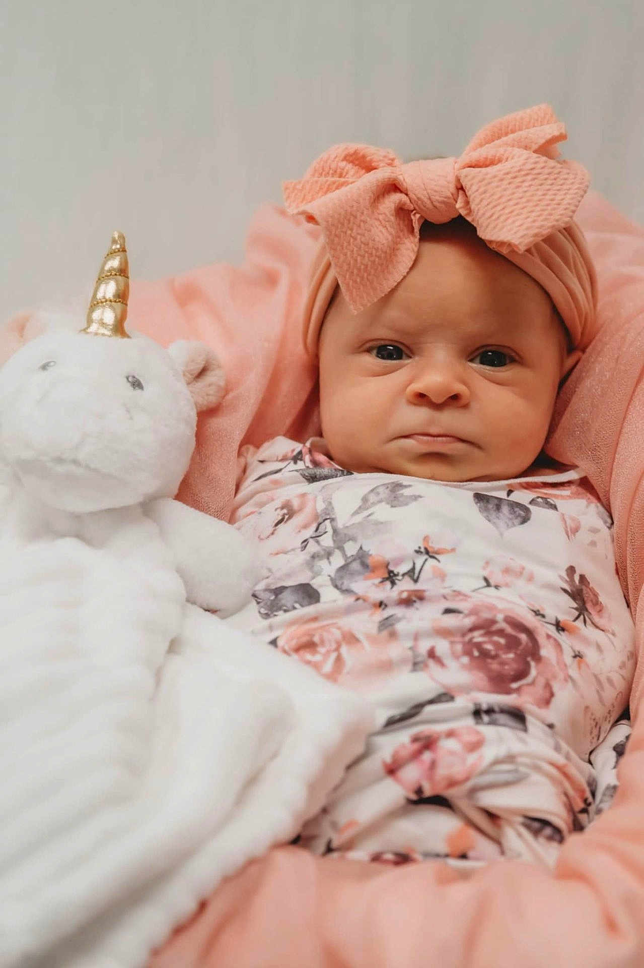 Emery joined the competition — help win amazing prizes! baby, infant, headband, bow, pink, floral_outfit, plush_toy, unicorn, blanket, soft_toy, cute, portrait, indoors, child, face, expression, newborn, cozy, resting, person