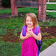 Nevaeh is registered to the contest to win money with this photo: child, girl, backpack, dress, pink, sidewalk, school, building, brick, sign, greenery, plants, shoes, smile, happy, outdoor, daytime, casual, young, student
