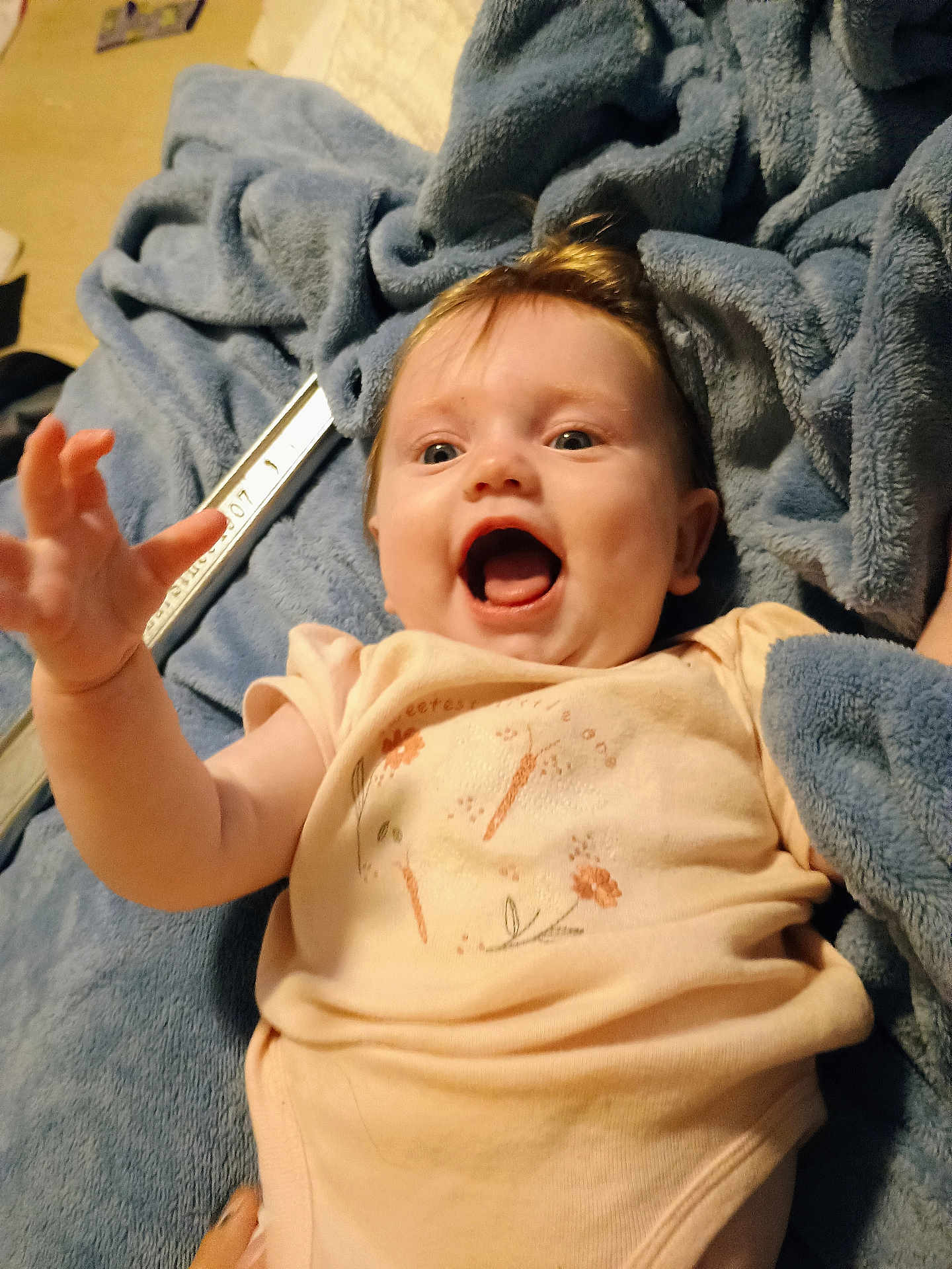 Briella joined the competition — help win amazing prizes! baby, infant, child, smiling, happy, blanket, blue_blanket, clothing, onesie, hand, face, portrait, indoor, cute, baby_girl, young_child, soft_texture, lying_down, reaching_hand, expression