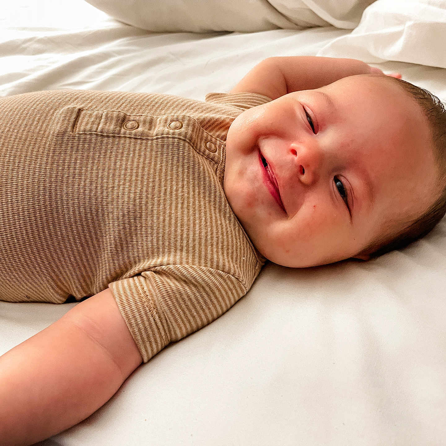 Rohen is registered to the contest to win money with this photo: arm, baby, bed, beige, cheeks, child, cute, face, happy, infant, lying_down, onesie, portrait, resting, skin, sleepwear, smiling, soft_light, striped, white_bed