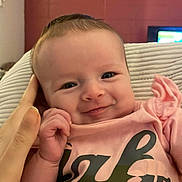Anna is registered to the contest to win money with this photo: baby, infant, smile, face, hand, pink_shirt, person, cute, indoors, portrait, child, human, clothing, expression, young, cozy, background, skin, head, eyes