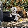 cat, black_cat, skeleton_statue, wooden_sign, garden, plants, outdoor, deck, leaves, sunlight, shadow, relaxing_cat, decor, whiskers, green_eyes, wood, nature, daylight, funny, animal