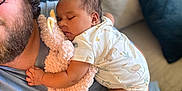 Charlotte joined the competition — help win amazing prizes! baby, sleeping, stuffed_animal, couch, adult, hand, controller, clothing, pillow, living_room, comfort, relaxation, child, toy, person, face, home, casual, nap, toddler