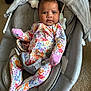 baby, infant, onesie, floral_pattern, baby_rocker, car_seat, gray, soft_fabric, indoor, carpet, child, person, newborn, cute, face, expression, sitting, comfortable, toy, pink_mittens