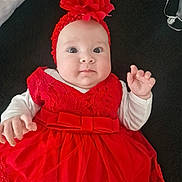 Ashley joined the competition — help win amazing prizes! baby, child, red_dress, headband, flower, portrait, infant, cute, face, hands, white_sleeves, lying_down, textile, fabric, close_up, young, person, indoors, fashion, adorable