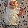 baby, infant, pacifier, hat, white_dress, lace, patterned_bedspread, blue_shorts, floral_pattern, socks, cute, lying_down, indoors, face, child, newborn, clothing, blanket, hand, portrait