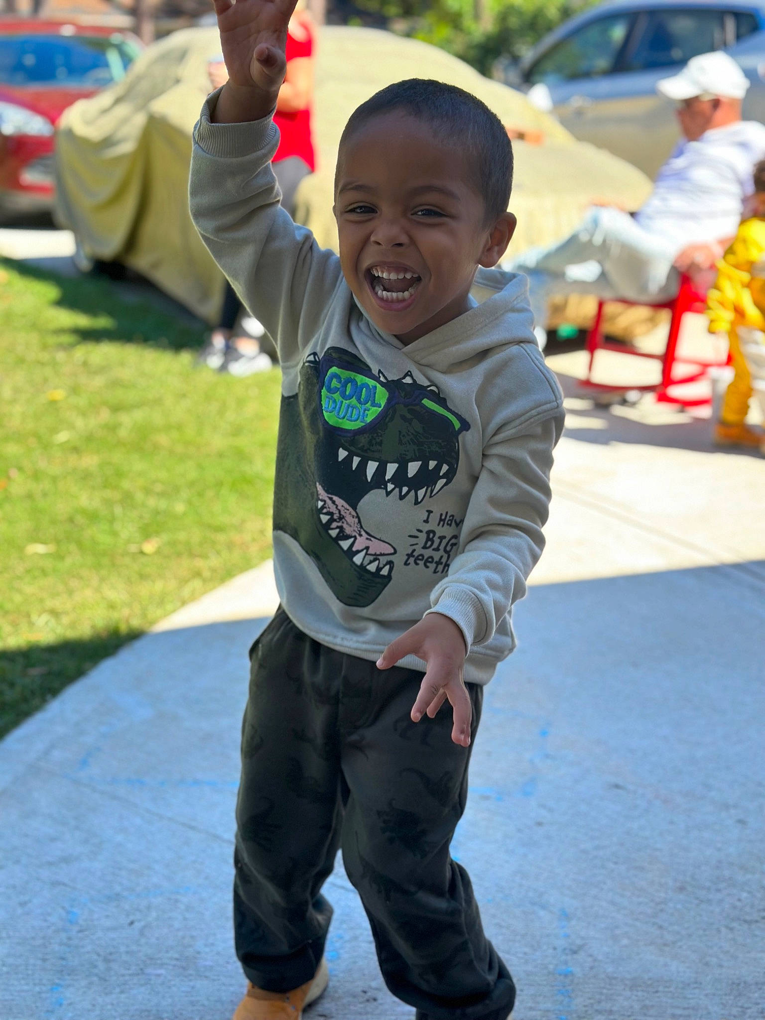 Kailer is registered to the contest to win money with this photo: car, child, event, face, fun, grass, happy, leisure, person, play, recreation, sitting, sleeve, smile, street, t_shirt, toddler, tradition, vacation, vertebrate