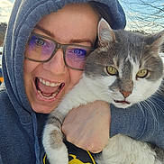 Frank joined the competition — help win amazing prizes! cat, person, selfie, portrait, outdoor, winter, hoodie, glasses, smiling, open_mouth, gray_cat, white_fur, tabby, whiskers, yellow_eyes, hugging, closeup, sky, trees, happy