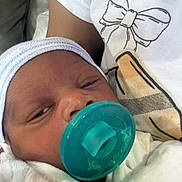 Royal is registered to the contest to win money with this photo: newborn, baby, infant, sleepy, pacifier, blanket, cap, swaddled, portrait, close_up, face, eyes, nose, mouth, cozy, indoors, clothing, white_shirt, bow_pattern, bedding