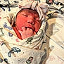 newborn, baby, infant, wrapped, blanket, footprint_pattern, hat, bow, sleeping, fingers_in_mouth, closeup, face, skin, cute, cozy, hospital_blanket, soft_lighting, peaceful, child, portrait