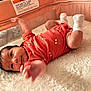 Lysandra is registered to the contest to win money with this photo: baby, infant, onesie, orange_clothing, cherry_pattern, playpen, mesh_sides, fluffy_blanket, reaching_hand, curious_expression, lying_down, indoor, soft_texture, newborn, cute, child, infant_care, baby_garment, small_arms, white_socks
