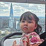 child, toddler, stroller, cityscape, skyscraper, cloudy_sky, urban, baby, pink_tutu, floral_top, hand, face, hair, earrings, window, railing, outdoor, portrait, curious, seatbelt