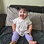 baby, child, smiling, sitting, pigtails, polka_dot, shirt, pants, lavender, cartoon_character, couch, blanket, happy, indoors, cute, face, feet, furniture, home, portrait