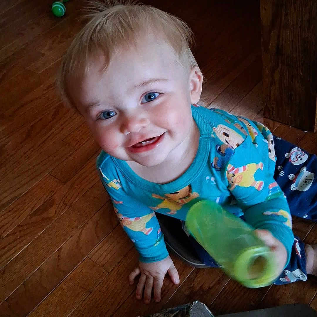 Kelver is registered to the contest to win money with this photo: toddler, child, smiling, blue_eyes, blonde_hair, bottle, sandal, wooden_floor, toy, colorful_pajamas, indoor, cute, happy, playing, person, flooring, casual, home, portrait, baby