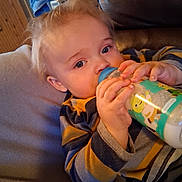 Kelver joined the competition — help win amazing prizes! toddler, child, baby_bottle, drinking, striped_clothing, blonde_hair, indoor, cozy, soft_furniture, leather_chair, hand, face, blue_eyes, casual_wear, relaxing, portrait, milk, cute, young_child, home