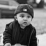 child, toddler, boy, cap, baseball_cap, toy_car, steering_wheel, black_and_white, outdoor, portrait, clothing, jacket, curious, expression, face, hand, young, cute, person, playing