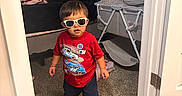 Christopher joined the competition — help win amazing prizes! toddler, child, sunglasses, red_shirt, car_print, barefoot, carpet, bedroom, crib, bed, blanket, pillow, door, door_hinge, flooring, toy, person, indoor, young_child, cool_kid