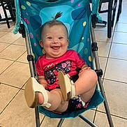 Lakelynn is registered to the contest to win money with this photo: baby, child, smiling, stroller, indoor, floor, tiles, shoes, happy, tongue_out, pink_shirt, blue_stroller, hair_tuft, furniture, chair, seat, playful, cute, person, infant