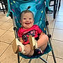 baby, child, smiling, stroller, indoor, floor, tiles, shoes, happy, tongue_out, pink_shirt, blue_stroller, hair_tuft, furniture, chair, seat, playful, cute, person, infant