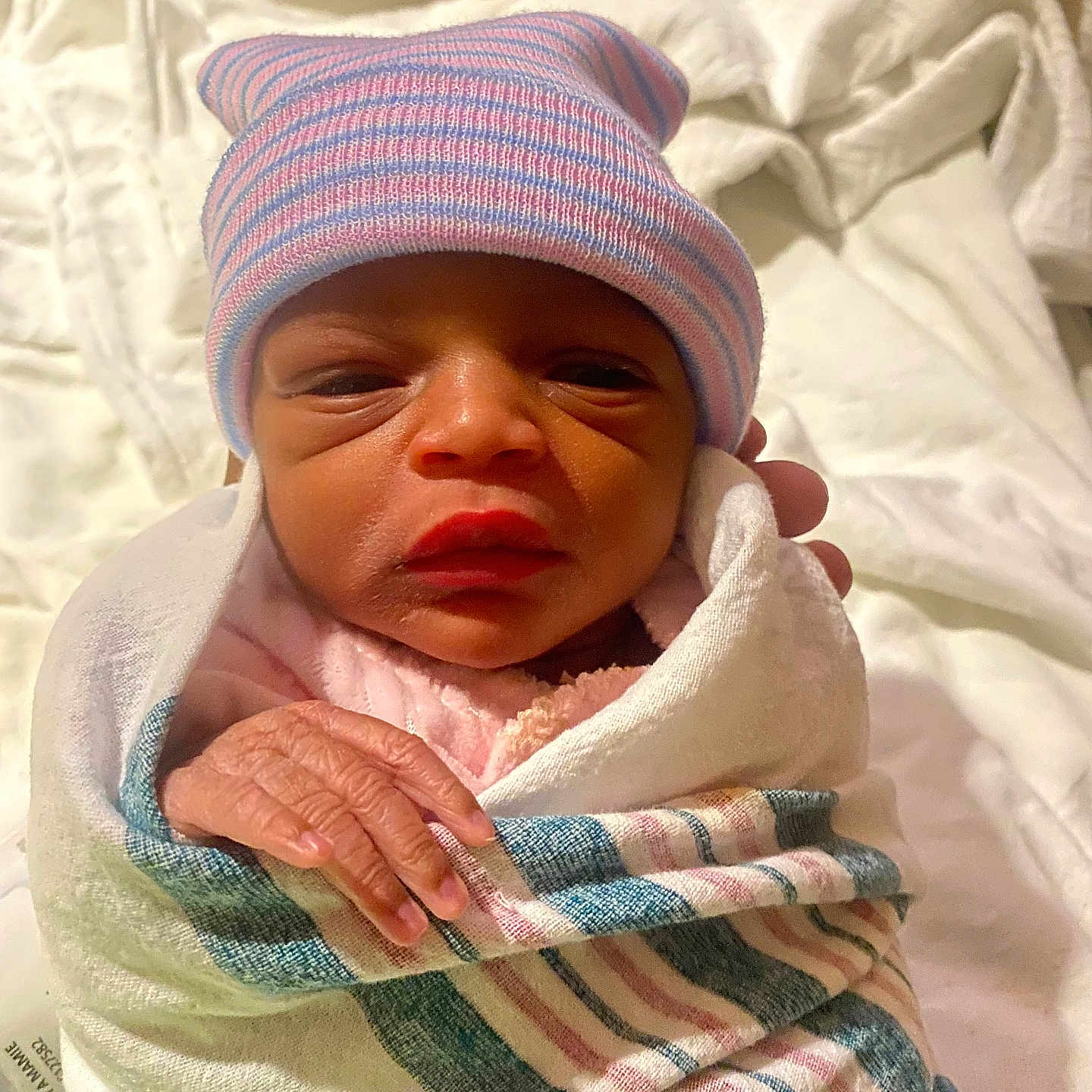 Janiyah joined the competition — help win amazing prizes! newborn, baby, infant, hospital, blanket, hat, striped_hat, wrapped, sleepy, hand, skin, person, portrait, cute, small, resting, indoors, cloth, headwear, human