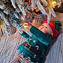 baby, christmas_tree, ornament, holiday, festive, elf_costume, striped_pants, knitted_blanket, lights, decorations, indoor, child, cute, celebration, winter, exploring, holiday_season, frosted_branches, infant, reaching