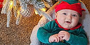 Casper is registered to the contest to win money with this photo: baby, child, christmas_tree, christmas_lights, ornament, holiday, festive_clothing, elf_costume, striped_pants, blanket, carpet, indoor, decorations, smiling, face, feet, knitted, cozy, happy, seasonal