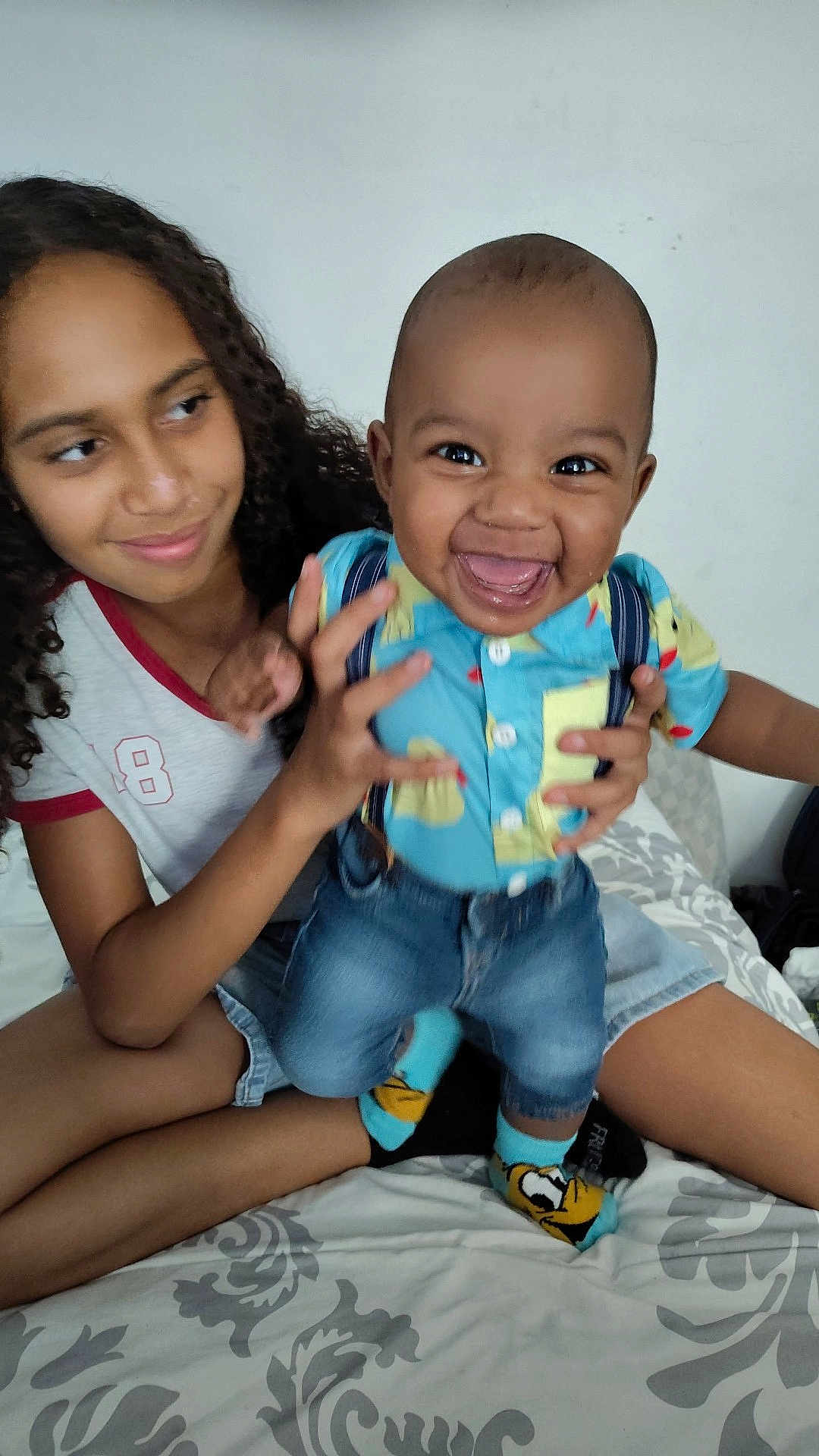 Avaughn is registered to the contest to win money with this photo: baby, bed, casual, child, clothing, curly_hair, cute, denim_shorts, fun, happy, holding, indoor, patterned_bedspread, person, playing, portrait, sibling, smile, socks, toddler