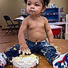 toddler, child, cake, messy, birthday, indoor, table, pigtails, jeans, sneakers, sprinkles, frosting, crumbs, playful, smudged_face, happy, chair, clock, shelf, wooden_floor
