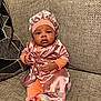 baby, infant, child, pink_clothing, bonnet, pacifier, sitting, couch, fabric, texture, cute, indoors, portrait, expression, soft_lighting, hand, footwear, person, home, relaxed