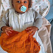 Louann participe au concours pour gagner de l'argent avec cette photo : baby, infant, pacifier, blanket, sleeping_sack, orange_blanket, bed, soft_toys, child, cute, indoors, cozy, clothing, face, hands, portrait, looking_up, resting, comfort, sleepwear