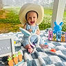 Tatem is registered to the contest to win money with this photo: baby, cowboy_hat, blanket, outdoor, grass, trees, toy, bunny_ears, carrots, easter_decor, smiling, child, cute, plush, colorful, sunlight, person, portrait, happy, nature