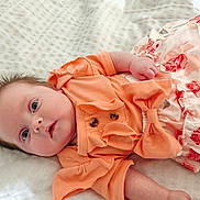 Sienna joined the competition — help win amazing prizes! baby, infant, child, face, blue_eyes, orange_clothing, floral_skirt, blanket, lying_down, cute, adorable, skin, hand, portrait, young_child, head, expression, indoor, soft_light, newborn