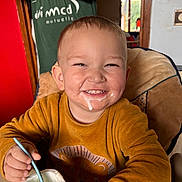Jules a rejoint le concours — aidez-le/la à gagner de superbes lots ! adult, arms_crossed, child, cute, dining, doorway, face, food, furniture, happy, high_chair, indoor, messy_face, orange_sweater, person, smile, spoon, toddler, window, yogurt