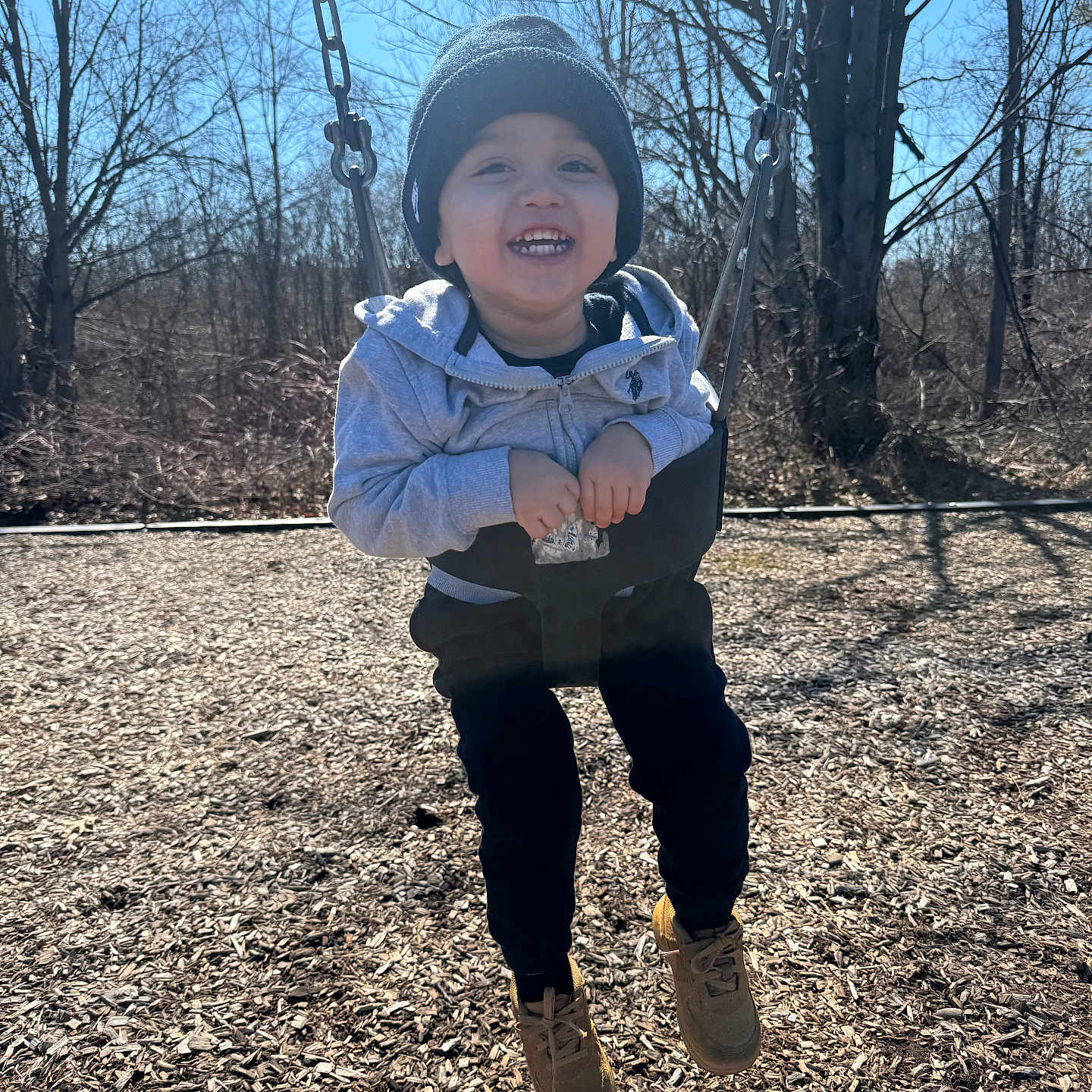Dario joined the competition — help win amazing prizes! child, toddler, swing, playground, outdoor, smiling, happy, clothing, hoodie, beanie, shoes, tree, woodchips, sunny, sky, nature, person, fun, play, winter