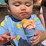 toddler, child, ice_cream, blue_shirt, banana_pattern, yellow_shorts, curly_hair, outdoor, sunlight, messy_face, hand, wicker_chair, person, summer, food, snack, cute, pensive, baby, playful