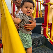 Dario joined the competition — help win amazing prizes! adult, barefoot, child, clothing, curly_hair, daylight, handrail, hat, holding, outdoor, people, playground, red, shirt, shorts, slide, smiling, stairs, toddler, yellow