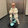 Mélyann participe au concours pour gagner de l'argent avec cette photo : toddler, child, scooter, sunglasses, vest, shoes, indoor, floor_tiles, elevator, metal_door, smiling, happy, play, toy, person, casual_clothing, modern, young_child, standing, cool