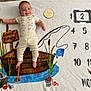 baby, infant, smiling, milestone_blanket, two_months, fishing_theme, boat, fish, reeds, clothing, striped_pants, onesie, lying_down, happy, cute, face, hand, feet, indoor, soft_texture