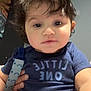baby, blue_clothing, child, close_up, clothing, curly_hair, cute, expression, face, hand, holding, indoor, infant, onesie, pacifier, person, portrait, seated, skin, young_child