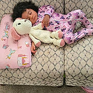 Neena joined the competition — help win amazing prizes! child, toddler, sleeping, pajamas, toy, stuffed_animal, couch, pillow, blanket, carpet, indoor, cozy, knitted_toy, purple, patterned, curly_hair, relaxing, home, comfort, nap