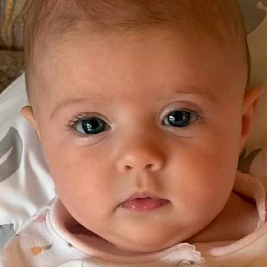 Aria joined the competition — help win amazing prizes! baby, infant, face, portrait, closeup, child, cute, eyes, expression, onesie, clothing, pattern, skin, head, young, person, resting, indoor, cozy, softlight