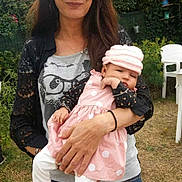 Leyla a rejoint le concours — aidez-le/la à gagner de superbes lots ! woman, baby, child, outdoor, garden, pink_dress, hat, holding, person, nature, greenery, white_chair, casual_clothing, long_hair, sleepy, polka_dot, leggings, adult, grass, daylight