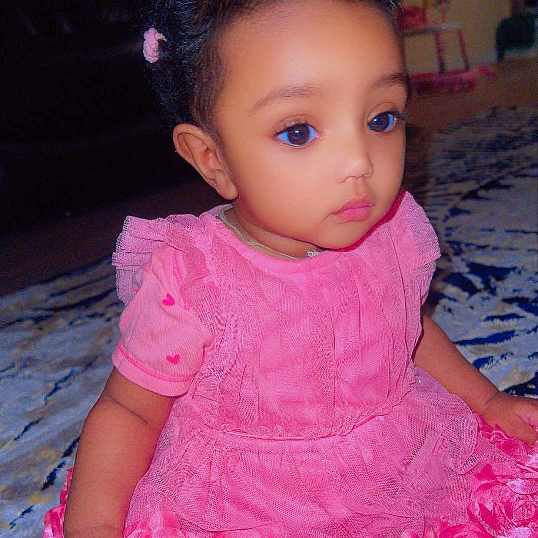 Sosayt is registered to the contest to win money with this photo: baby, child, toddler, portrait, sitting, pink_dress, ruffles, floral_dress, hair_bows, hair_accessories, wide_eyed, serious_expression, indoors, living_room, carpet, furniture, close_up, photography, fashion, cute