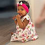baby, child, girl, headband, bow, floral_dress, sitting, floor, indoors, curly_hair, cute, playful, chewing, card, portrait, skin, happy, young_child, one_person, closeup