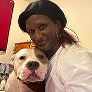 Blessed is registered to the contest to win money with this photo: person, dog, indoor, white_shirt, smile, hug, curtain, dresser, shoes, bedroom, face, earrings, black_hair, light_skin, pet, friendly, closeup, portrait, animal, home