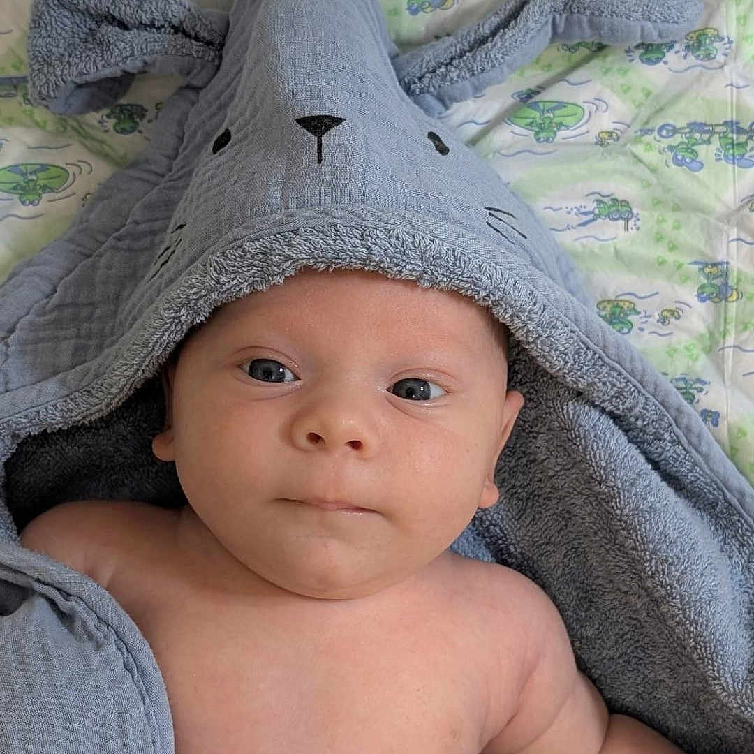 Liam a rejoint le concours — aidez-le/la à gagner de superbes lots ! baby, blanket, blue, bunny_ears, child, comfort, cute, expression, eyes, face, indoors, infant, lying_down, pattern, portrait, skin, soft, towel, wrapped, young