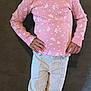 child, girl, pink_shirt, floral_pattern, curly_hair, pigtails, cream_pants, pink_sneakers, standing, posing, hands_on_hips, smiling, indoor, concrete_floor, dark_wall, casual_clothing, portrait, fashion, young, cute