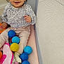 toddler, child, smiling, curly_hair, blue_bow, playpen, plastic_balls, pink_blanket, sitting, happy, indoors, clothing, long_sleeve_shirt, pants, sock, face, person, toy, baby, cute