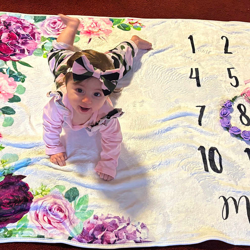 Josslyn joined the competition — help win amazing prizes! baby, child, milestone_blanket, flower_crown, headband, crawling, pink_clothing, floral_pattern, numbers, months, carpet, indoor, cute, smiling, portrait, young_child, baby_girl, colorful, decorative, soft_texture