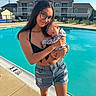 Leilani joined the competition — help win amazing prizes! woman, baby, pool, swimwear, shorts, glasses, outdoor, daytime, residential_building, lounge_chairs, water, holding, tenderness, summer, sky, clouds, concrete, fence, person, portrait